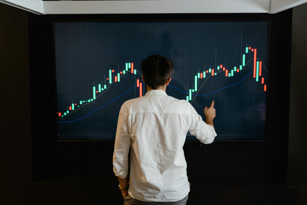 Adult male reviewing stock market data on a large display screen indoors.